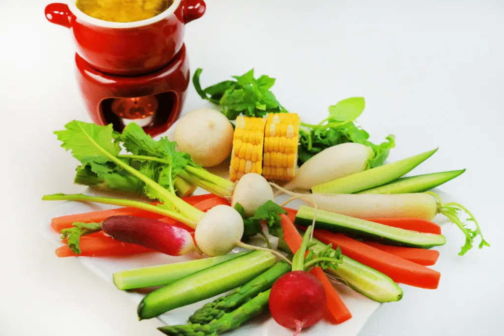 Ingredients for bagna cauda recipe laid out on a wooden board, including garlic, anchovies, olive oil, butter, and heavy cream.
