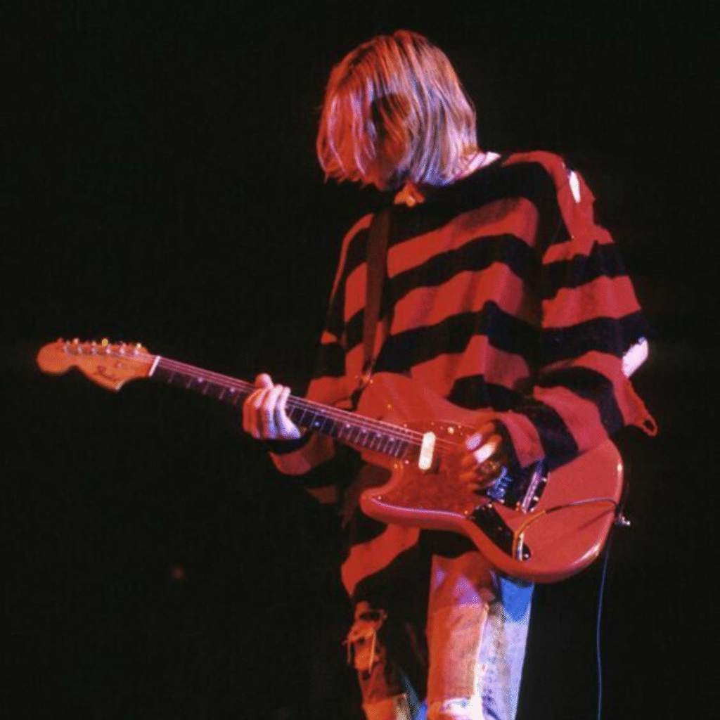Kurt Cobain performing on stage in classic grunge attire – ripped jeans and flannel shirt, 90s style icon