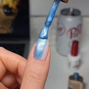 Applying blue cat eye nail polish as the first step to creating a magnetic cat eye nails design.