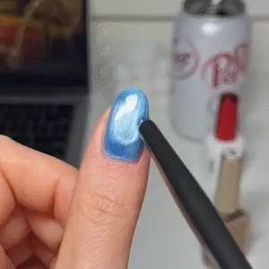 Using a nail magnet over wet polish to form the signature shimmer pattern in cat eye nails.
