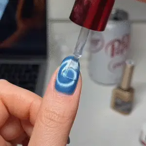 Applying a glossy top coat over cat eye nails to seal in the magnetic design and add shine.