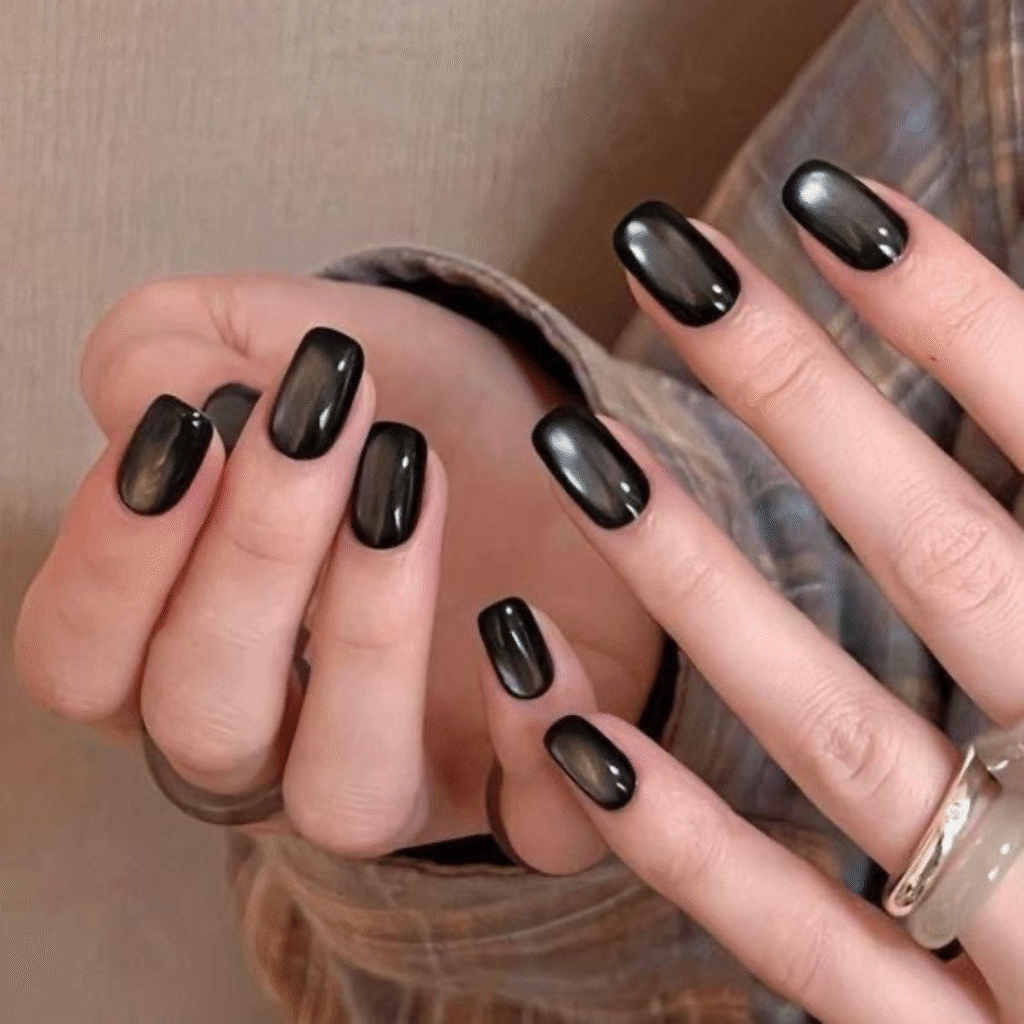Short coffin-shaped black cat eye nails with a metallic cosmic glow.