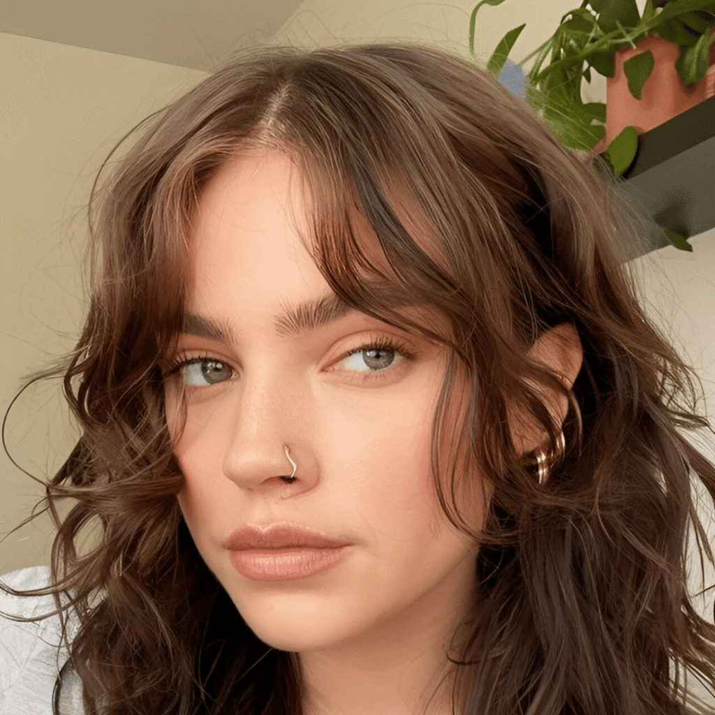Brunette woman with short, curly hair and soft curtain bangs framing her face naturally.