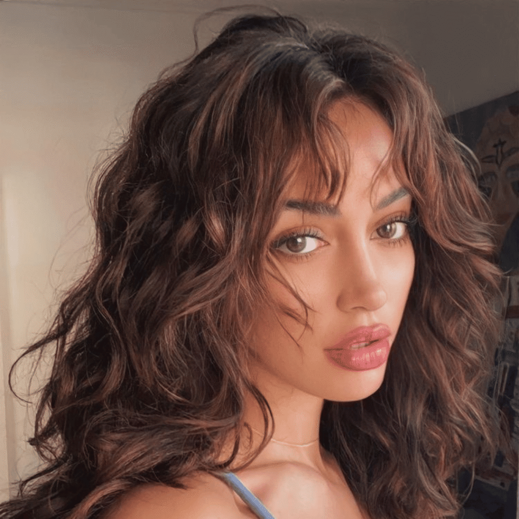 Dark brunette woman with naturally curly hair and layered curtain bangs turned slightly to the side.