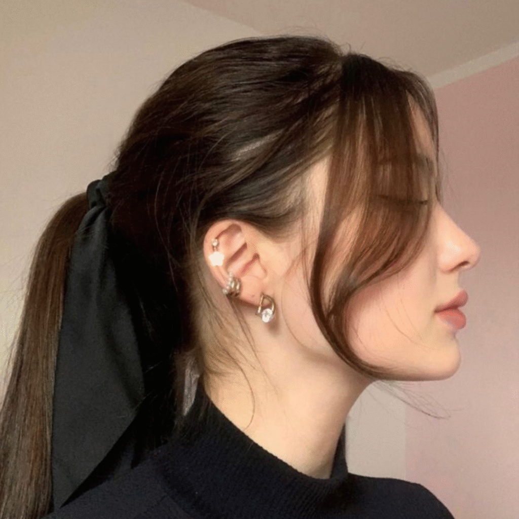Woman with a low ponytail, soft curtain bangs framing her face, and a bow accessory at the back.